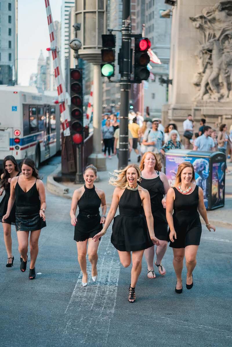 Six female friends on a bachelorette trip together crossing an intersection and laughing in Chicago, USA