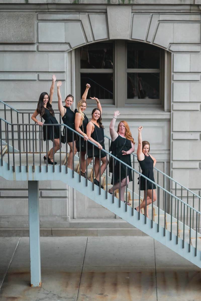 Six female friends on a bachelorette trip standing on some stairs raising their hands in the air in Chicago, USA