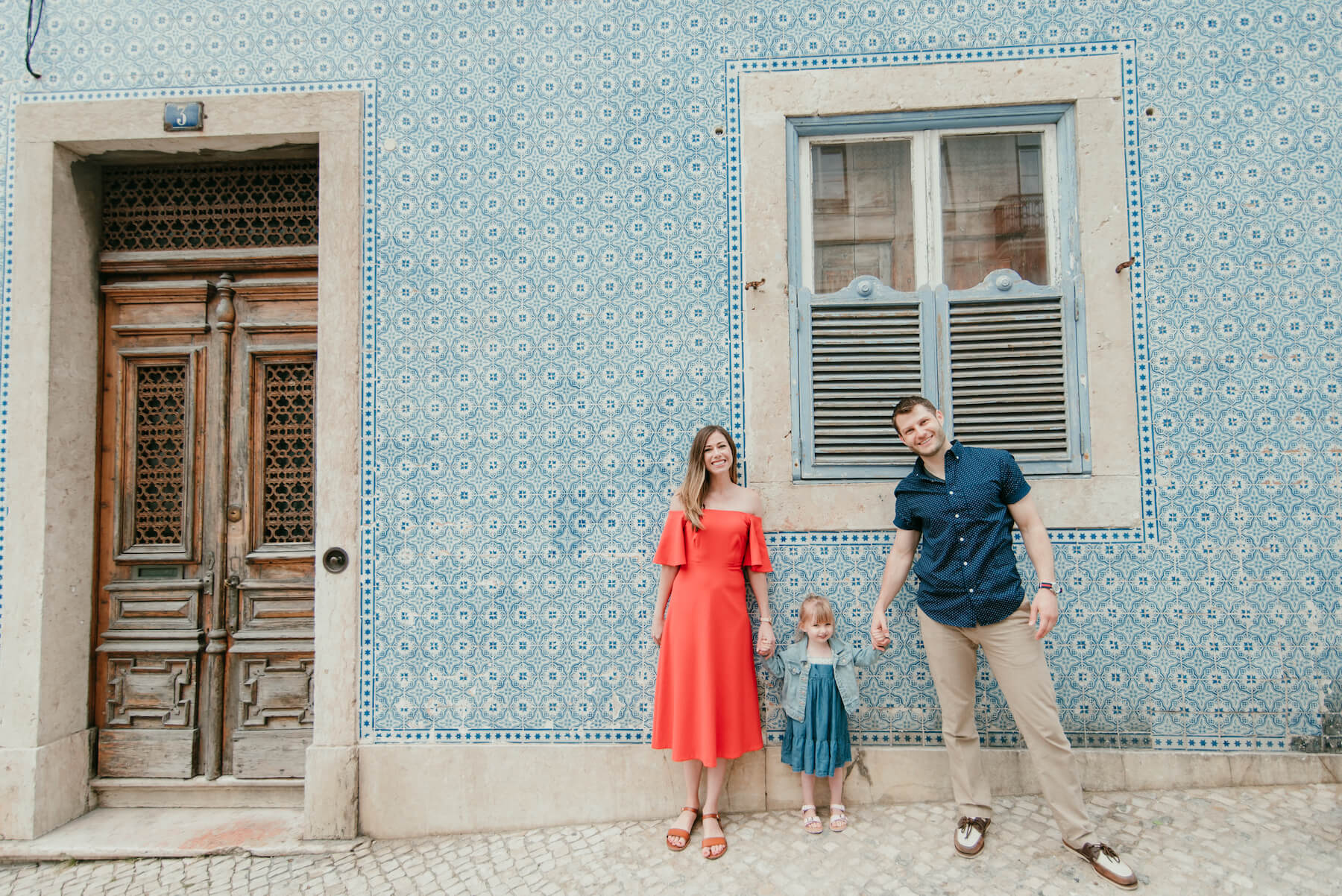 a family of 3 standing with their young child in front of a colourful wall in Lisbon, Portugal