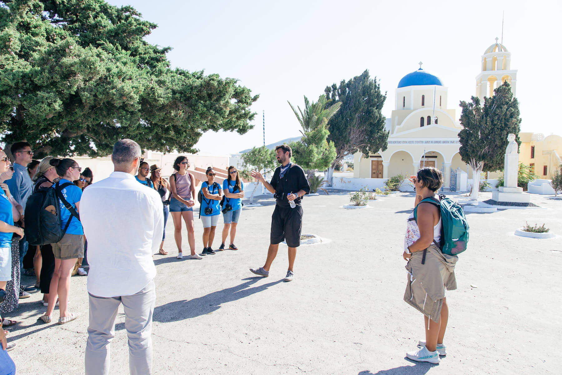 Photographers in a group listening to a speaker in public square in Santorini, Greece.