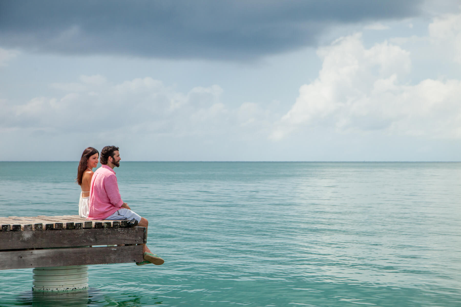 couple sitting on the edge of a dock looking out into the ocean in Placencia, Belize