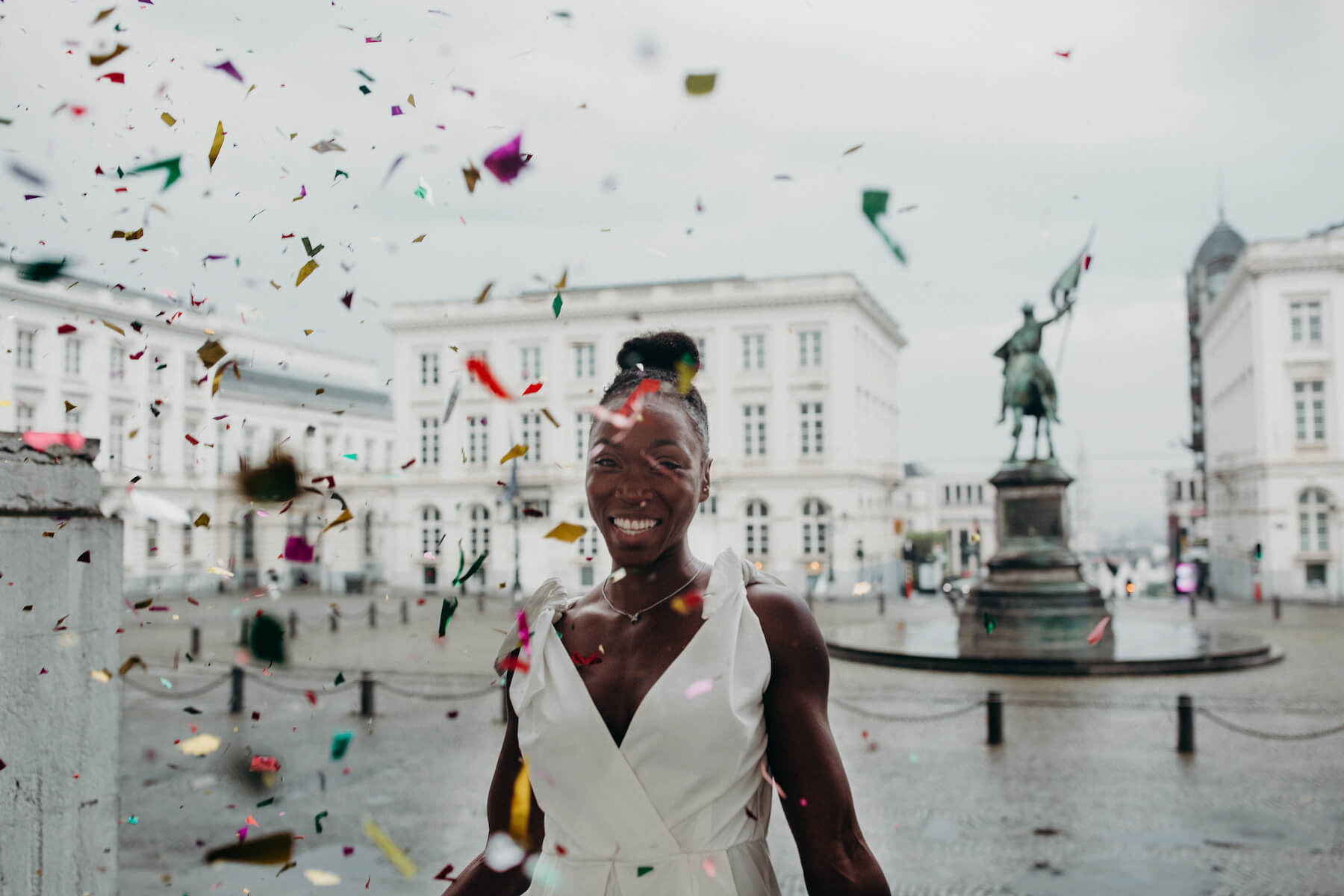 A woman celebrating her birthday with confetti and gold balloons wearing a white dress on a photoshoot with Flytographer.