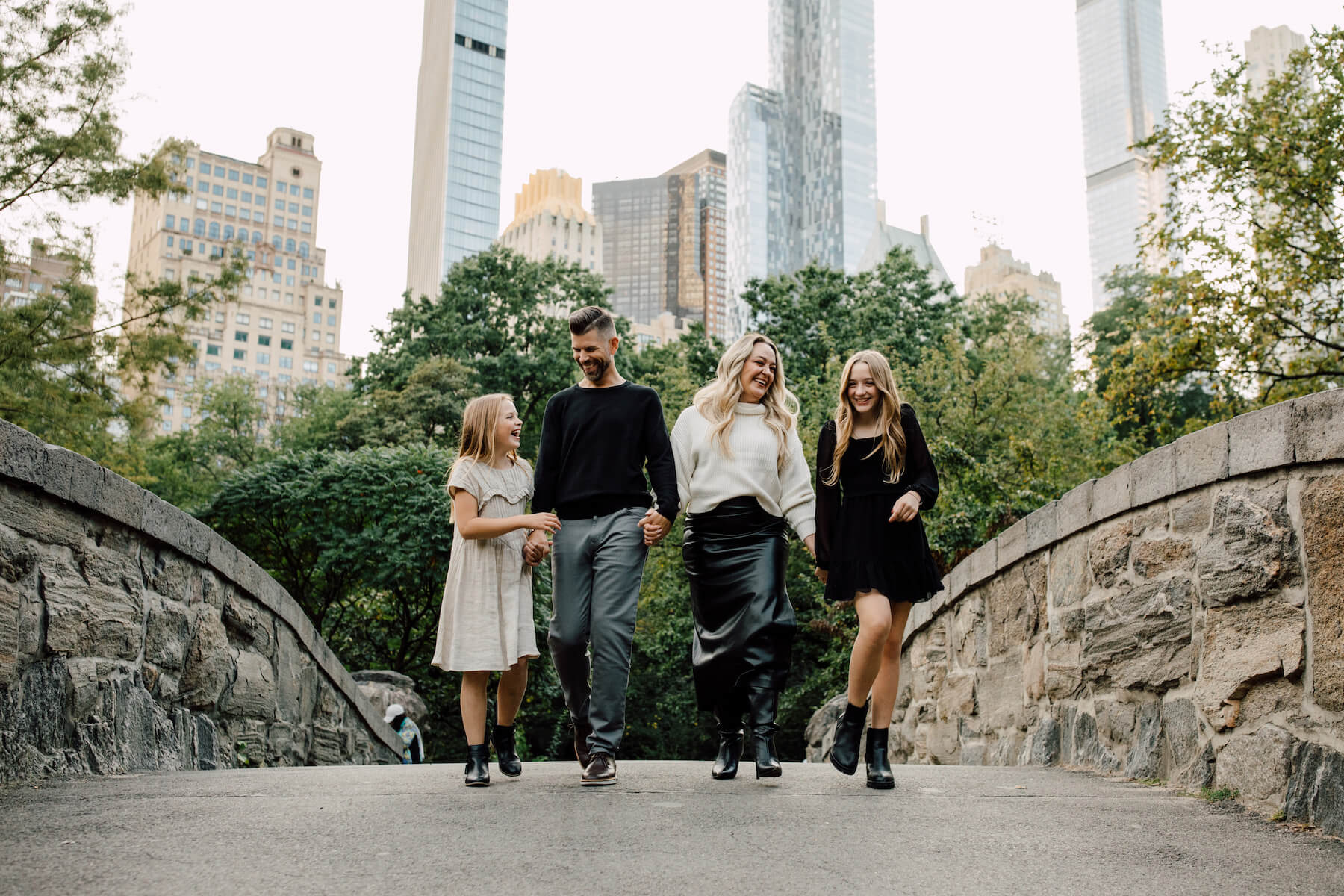 A family walks across Gapstow Bridge holding hands in New York City while on a family photoshoot with Flytographer.